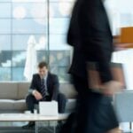 white man in suit sitting in a busy office