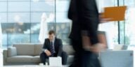 white man in suit sitting in a busy office