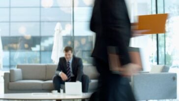 white man in suit sitting in a busy office