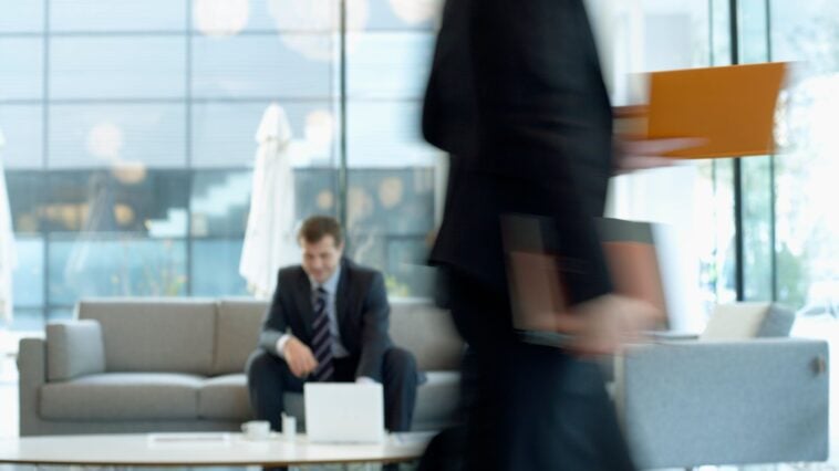 white man in suit sitting in a busy office