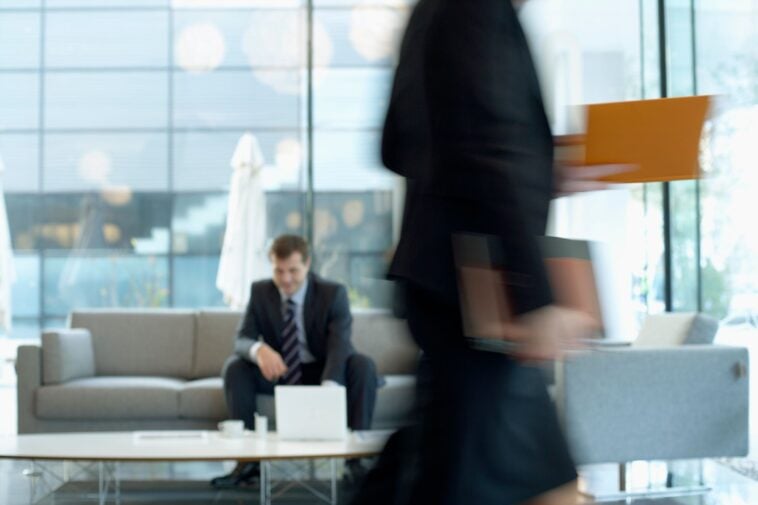 white man in suit sitting in a busy office